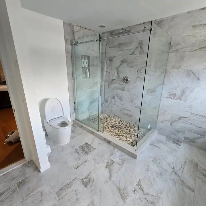 Corner shower with a glass panel and a pebble mosaic floor in marble-look walls