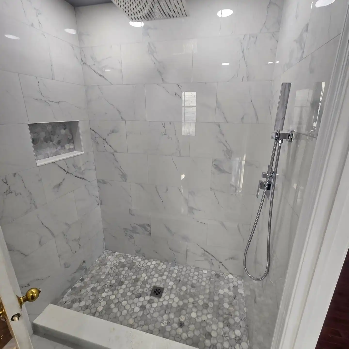 Walk-in shower in large-format marble-look porcelain with black fixtures and a hexagon mosaic floor