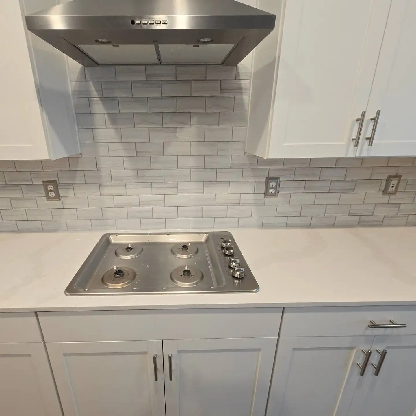 Grey subway tile backsplash behind a gas cooktop under a stainless hood