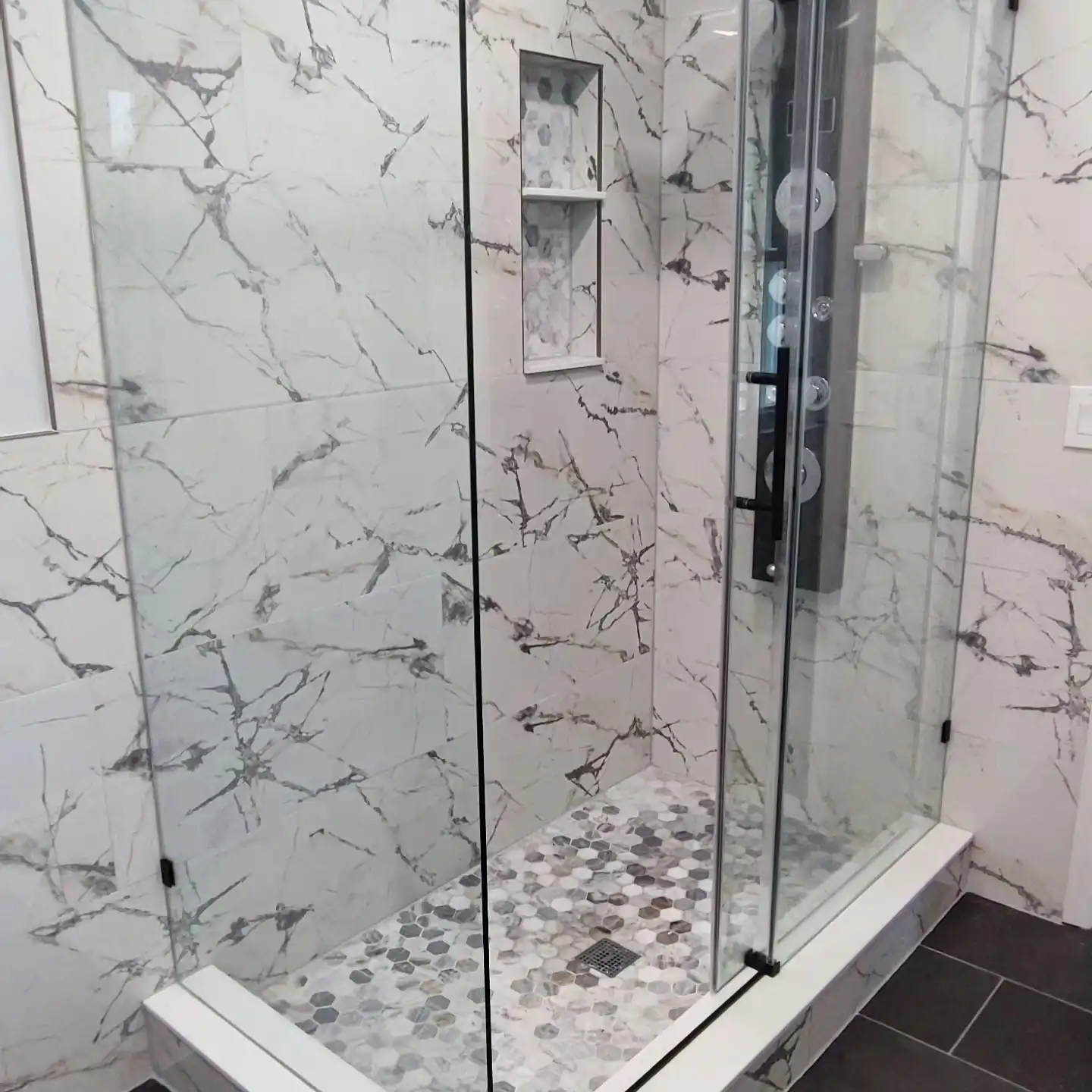 The finished shower in marble-look porcelain with a hexagon floor and glass door