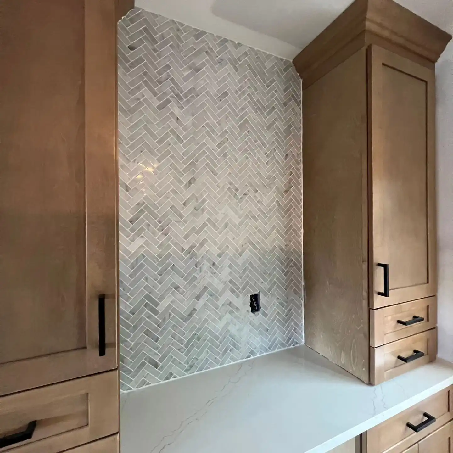 Herringbone marble backsplash between oak upper cabinets and a white quartz counter