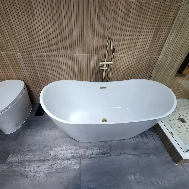 White freestanding tub with a floor-mounted gold filler on a concrete-look floor