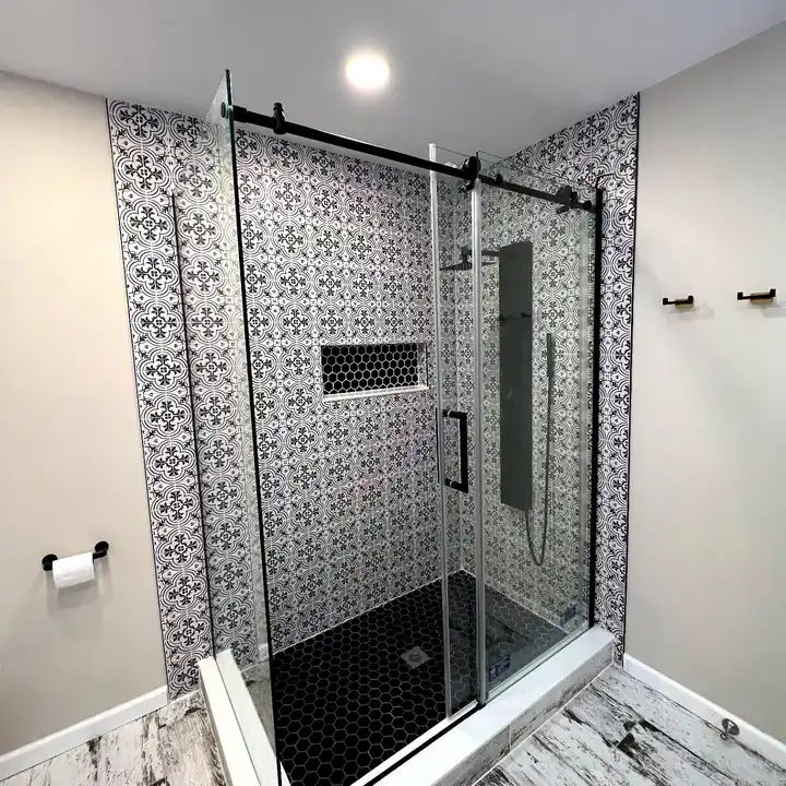 Black-framed sliding shower door in front of black and white patterned tile