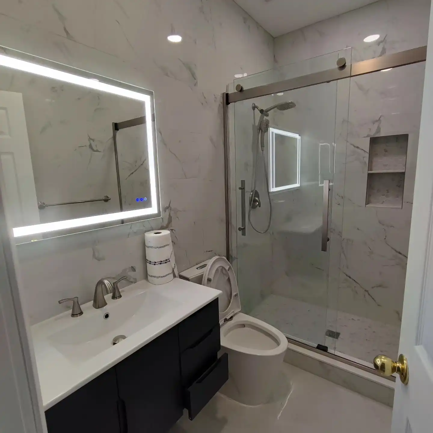 The same bathroom finished in marble-look porcelain with an LED mirror