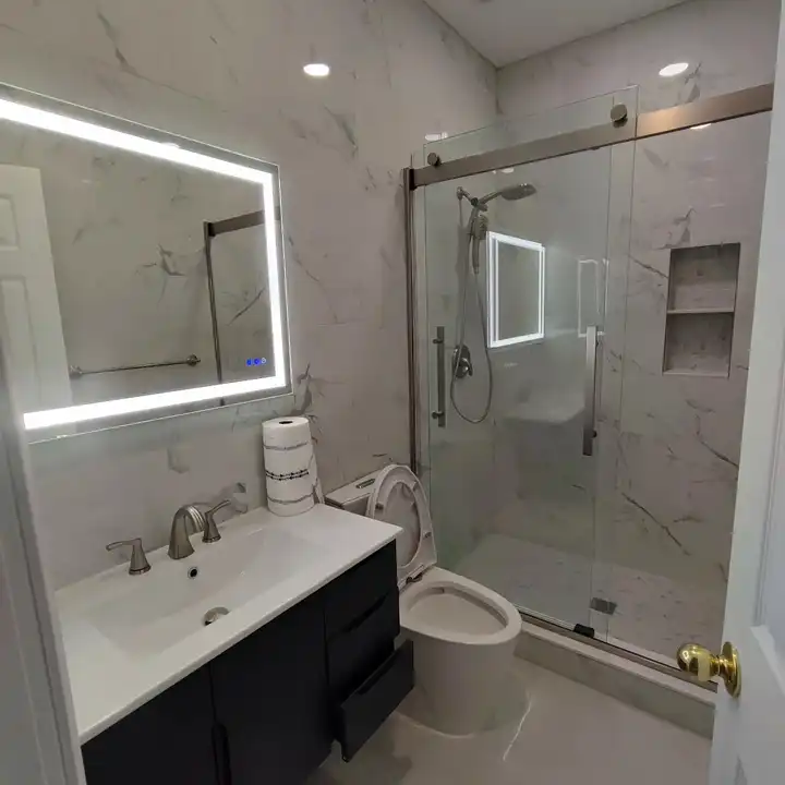 Marble-look hall bath with an LED mirror, black vanity and a sliding glass shower